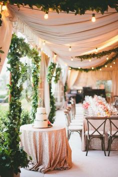 a table with a cake sitting on top of it under a canopy covered in greenery