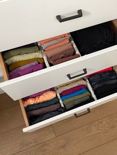 an open drawer with clothes in it on top of a wooden floor next to a wall