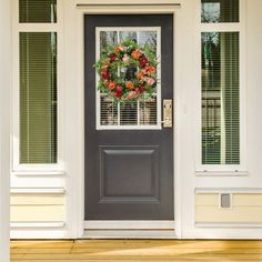 a wreath on the front door of a house with shutters and flowers in it