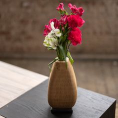 a vase filled with pink and white flowers on top of a wooden table next to a brick wall