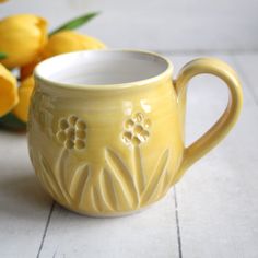 a yellow coffee cup sitting on top of a table next to some tulips