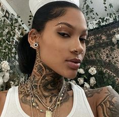 a woman with tattoos and piercings on her neck wearing a white tank top is looking at the camera