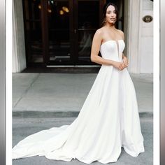 a woman in a white wedding dress standing on the sidewalk