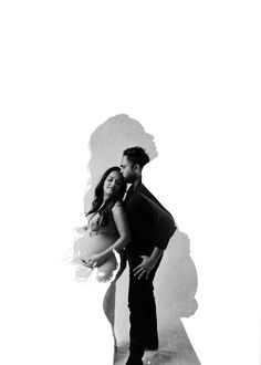 black and white photo of a man and woman embracing each other in front of a wall