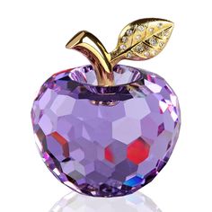 an apple with a leaf on it is shown in gold and purple colors, sitting on a white surface