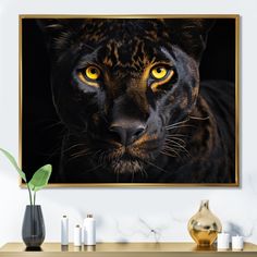 a framed photograph of a black leopard with yellow eyes on a wall next to candles and vases