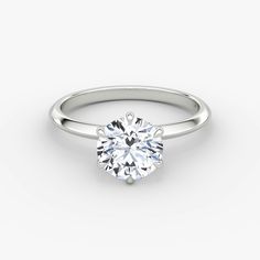 a white gold ring with a round brilliant cut diamond in the center, on a plain surface