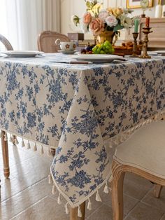 a dining room table with a blue and white floral design on the table cloth that has tassels around it