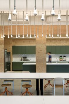 an open kitchen and dining area with stools in front of the counter, lights hanging from the ceiling