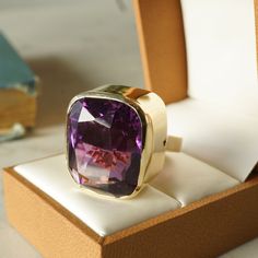 Bezel Set Amethyst Cocktail Ring in 14k Yellow Gold. From the Ancient Egyptians to the Middle Ages and beyond, amethysts have been a highly sought after gemstone with a vast history of international folklore and symbolism. This one of a kind cocktail ring features a 35.41 carat cushion cut purple amethyst finished in 14K yellow gold. The amethyst has a vibrant, dark violet hue. The center stone is bezel set on polished yellow gold band. Composition: 14 Karat Yellow Gold Era: Modern 1970 - Presen Luxury Yellow Gold Amethyst Ring With Bezel Setting, Luxury Purple Ring With Bezel Setting, Luxury Amethyst Gemstones For Gift, Luxury Amethyst Gemstones As Gift, Luxury Faceted Amethyst Ring For Formal Occasions, Luxury Faceted Amethyst Ring For Formal Events, Formal Amethyst Ring With Large Stone, Formal Yellow Gold Amethyst Ring With Bezel Setting, Luxury Polished Amethyst Ring