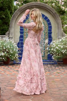 a woman in a long pink dress standing on a brick walkway with flowers around her