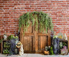 an old wooden door surrounded by plants and other decorations on display in front of a brick wall