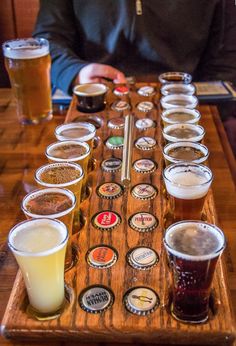 a wooden tray filled with lots of different types of beer glasses on top of a table