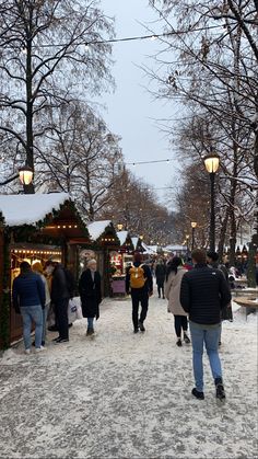 people are walking around in the snow near christmas decorations and lights on display at an outdoor market