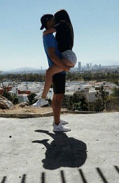 a man and woman kissing on the top of a hill with city in the background