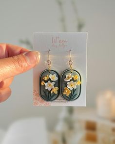 a hand holding up a pair of earrings with yellow flowers on the front and back