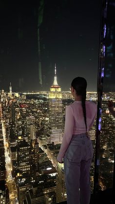 a woman standing on top of a tall building looking at the city lights and skyscrapers