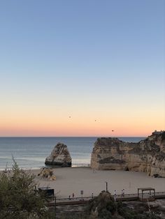 people are walking on the beach near some large rock formations at sunset or sunrise time