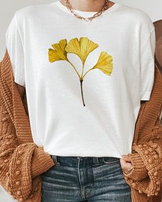 T-shirt featuring a botanical illustration of a fall Gingko leaf. Fall in love with our autumn leaf shirt you won't find anywhere else. Printed on a white cotton t-shirt, made from durable lightweight cotton. Unisex fit - boxy and long. How it's made: * All prints are original watercolor designs hand-painted by a botanical artist. * Ethically made 100% cotton t-shirts that are made to last. * T-shirts are printed and shipped by my printing partner in the US, Canada, or Europe. * By buying from this shop you are directly supporting a woman-owned small business, created out of love for plants to educate, inspire and keep us connected to the natural world. About the artist: This Shop is an extension of my botanical illustration studio, where I create hand-painted watercolor art for internatio Casual Fall Shirt With Plant Print, Casual Fall Tops With Plant Print, Yellow Graphic Print Shirt For Fall, Casual T-shirt With Plants Print For Fall, Casual Plants Print T-shirt For Fall, White Tops With Plant Print For Fall, Casual Fall T-shirt With Plant Print, White T-shirt With Fall Themed Plant Print, White T-shirt With Plant Print For Fall