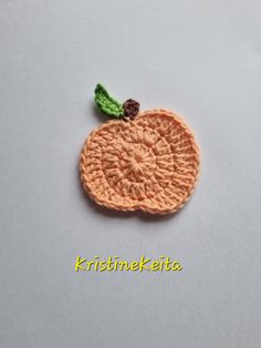 an orange crocheted brooch with a green leaf on the top and bottom