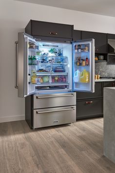 an open refrigerator in a kitchen with wooden flooring and gray cabinets, along with stainless steel appliances