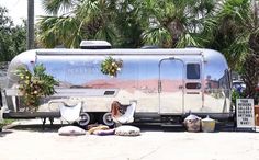 an airstream parked in front of palm trees and potted plants on the side