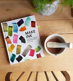 the book make ink is next to a cup of coffee and spoon on a wooden table