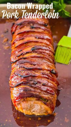 bacon wrapped pork tenderloin on a baking sheet with bbq sauce in the background