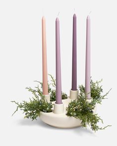 four candles are arranged in a bowl with greenery