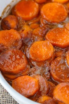 cooked carrots sit in a white dish on a tableclothed cloth, ready to be eaten