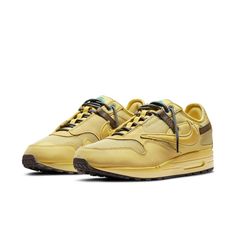 The Travis Scott x Nike Air Max 1 'Saturn Gold' is a must-have sneaker for any fan of the hip-hop artist. This sneaker features a monochrome yellow palette throughout the upper, giving the shoe a unique and attention-grabbing look. The upper is made from breathable mesh, with stitched leather overlays adding durability and a premium feel. Outdoor-inspired details include two-tone rope laces and brown webbing straps integrated into the laces and heel overlay. The tongue features a rubberized Cactus Jack patch, while Scott's trademark reverse Swoosh adorns the lateral side of the sneaker. Out of all the high-profile artist collaborators Nike has under their belt, Travis Scott is still one of the most notable figures, having worked on iconic silhouettes including the AJ 1s and AJ 4s while als Nike Travis Scott, Nike X Travis Scott, Travis Scott Cactus Jack, Low Air Jordan 1, Jordan 4s, Gold Sneakers, Jordan 12 Retro, Cactus Jack, Nike Air Max 1