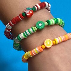 three bracelets with different colored beads and fruit designs on them, one for the woman's arm