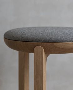 a close up of a wooden stool with grey fabric