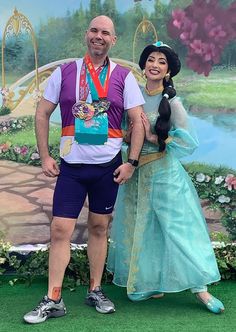 a man and woman standing next to each other in front of a disney character backdrop