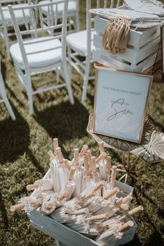 an outdoor ceremony with white chairs and wooden sticks in the grass, on which there is a sign that reads