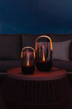 two glass vases sitting on top of a table next to a couch with pillows