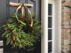 a wreath hanging on the front door of a house with pine cones and evergreens