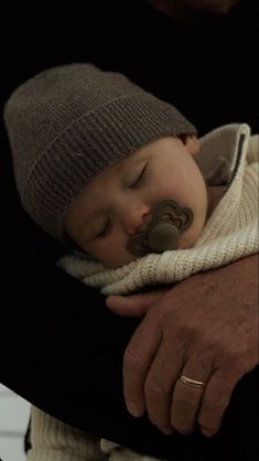 a man holding a baby with a pacifier in it's mouth while wearing a hat