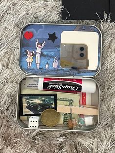 an open tin with some items in it on a furry surface next to a coin