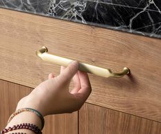 a person's hand holding onto a door handle on a wooden cabinet with marble counter top