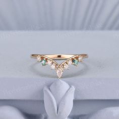 a gold ring with green and white stones sits on top of a white cloth napkin