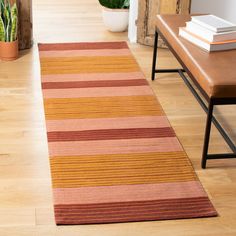 a striped rug is on the floor next to a wooden bench and potted plant