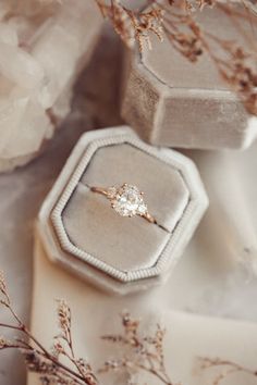 an engagement ring sitting on top of a white box next to some flowers and rocks