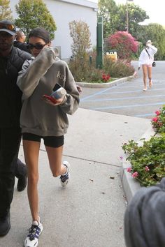 a woman walking down the sidewalk while holding onto a cell phone in her hand and another man standing behind her