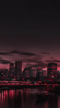 the city skyline is lit up at night with red lights in the foreground and dark clouds in the background