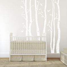 a baby's room with a crib, dresser and wall decal that has white birch trees on it