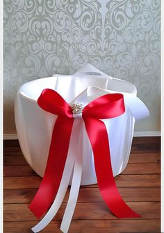 a white basket with red ribbon and a ring on it sitting on a wooden floor