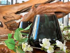 a black vase sitting on top of a wooden table next to white and green flowers