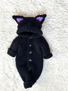 a knitted black cat sleeping bag on a white carpet with purple eyes and ears