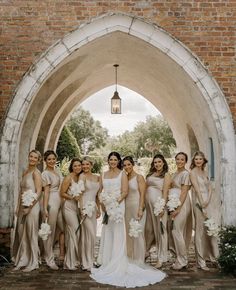 a group of women standing next to each other in front of a brick wall holding bouquets